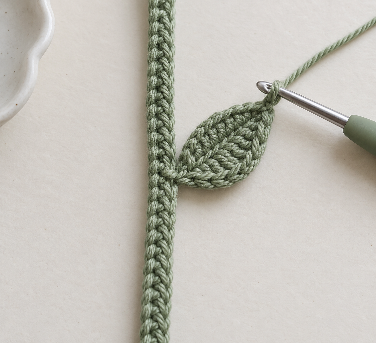 Sage-green crochet leaf attached to the side of a narrow bookmark stem with the hook at the leaf tip