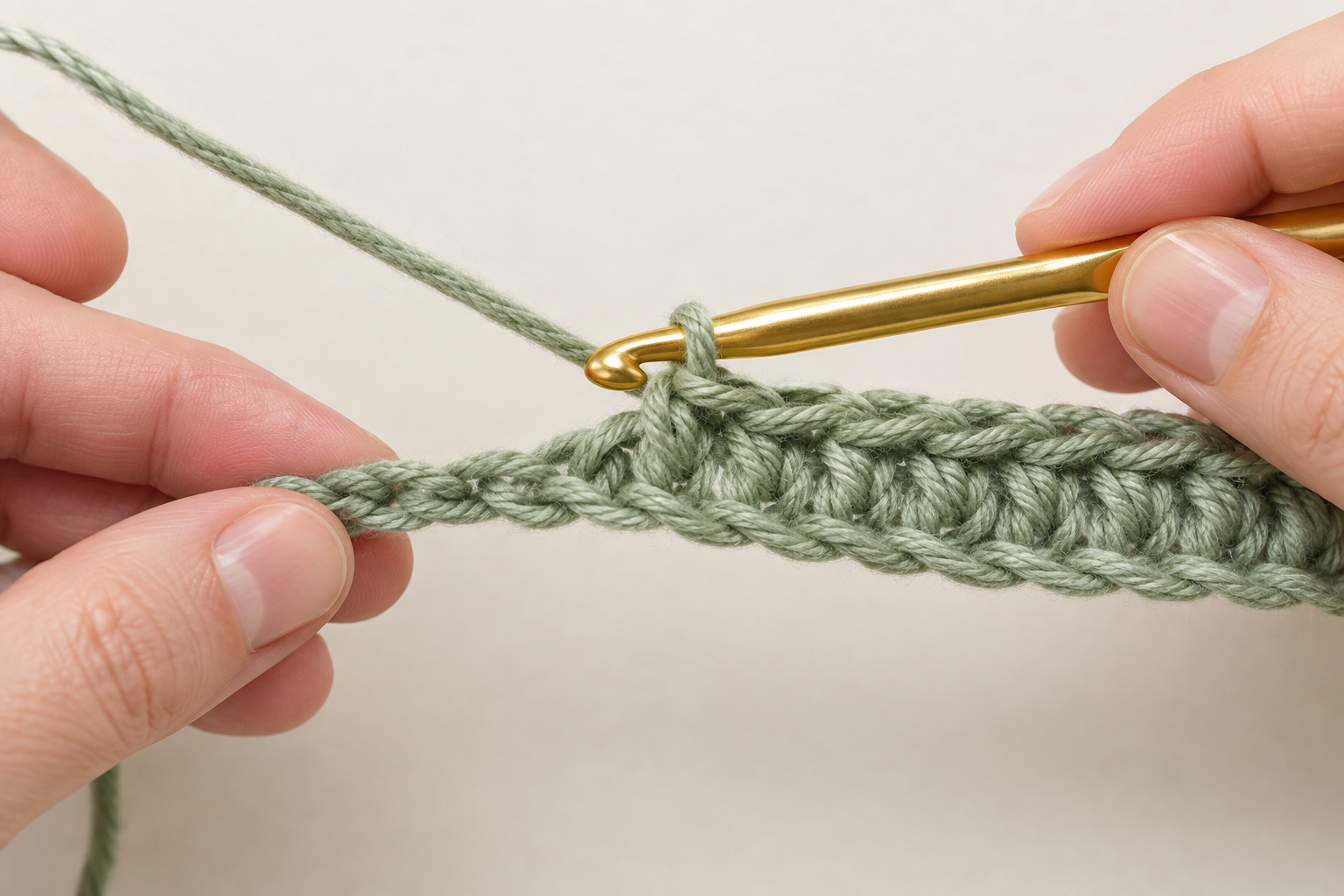 Gold crochet hook and sage green yarn at the first completed half double crochet scarf row