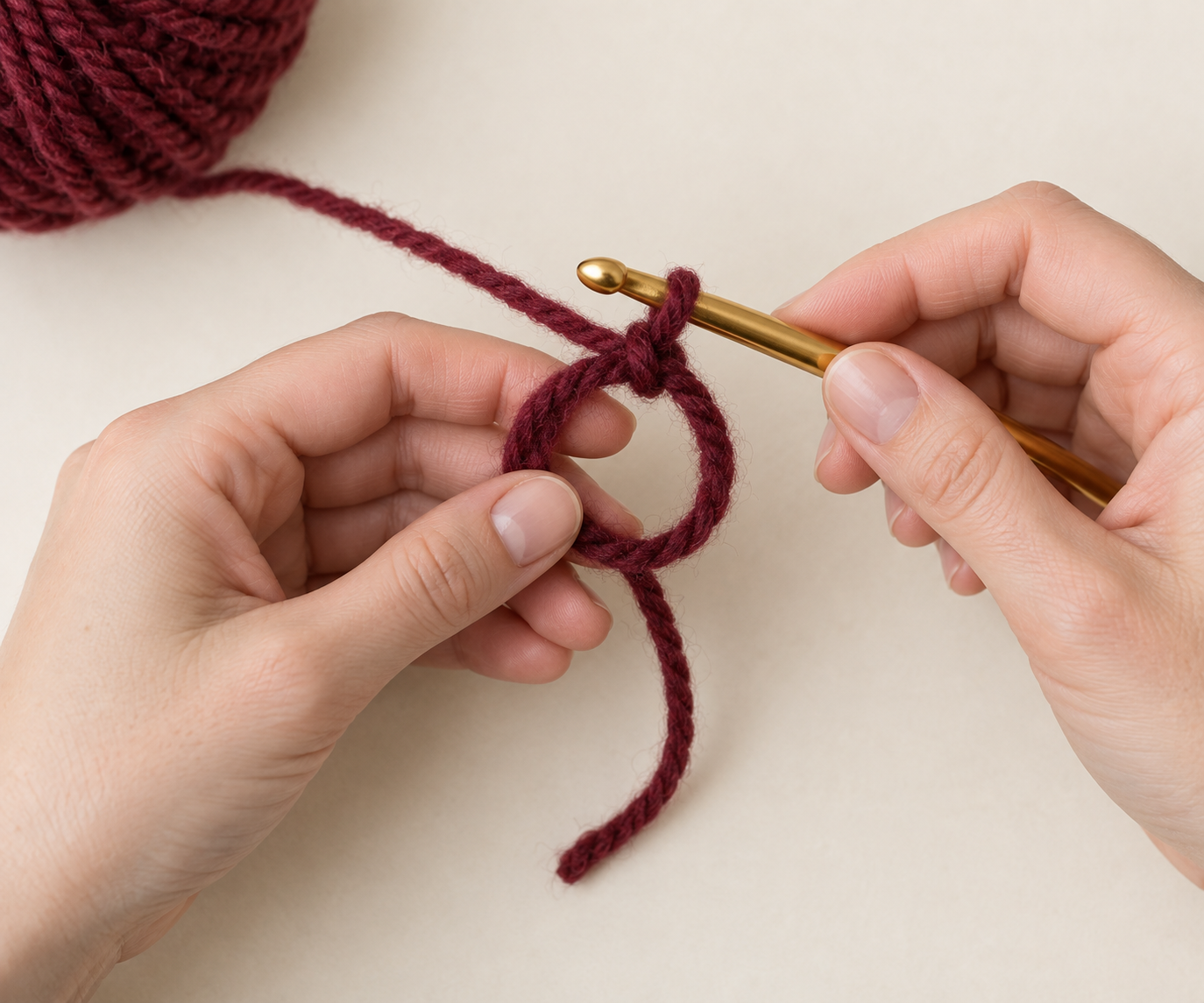 Burgundy chunky yarn formed into an open crochet magic ring with a gold hook